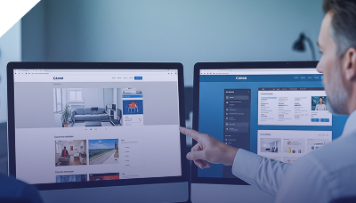 Developer pointing at dual monitors showing Canon website frontend and backend admin panel.
